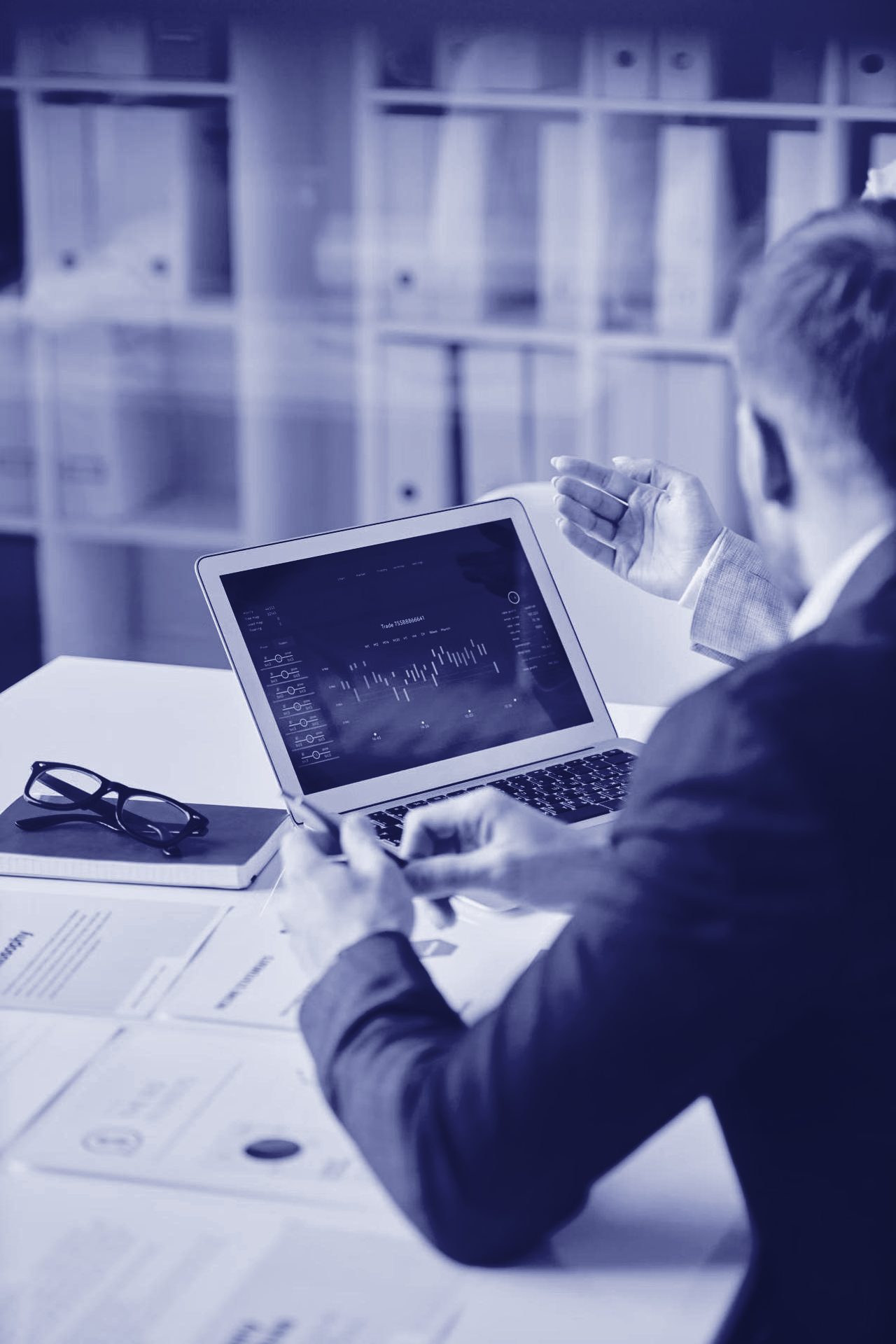 Economista analizando gráficos financieros en un portátil durante una reunión de trabajo